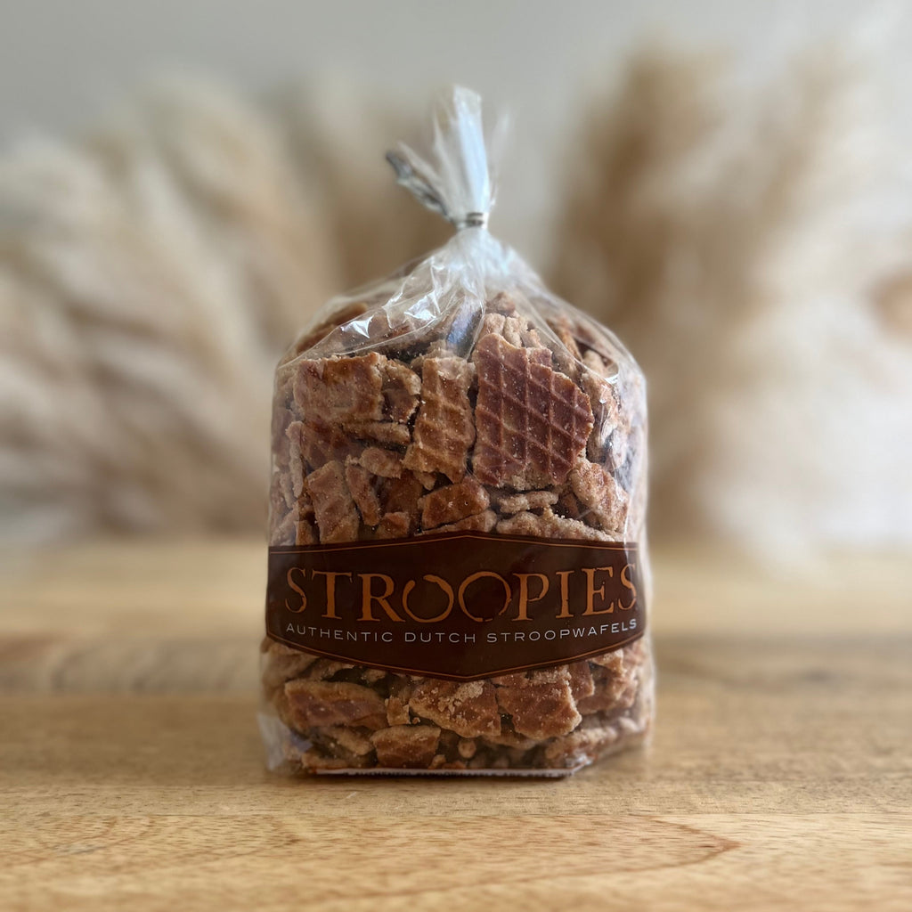 A clear plastic bag of Stroopies authentic Dutch stroopwafels, tied at the top, sitting on a wooden surface with a soft-focus background of dried pampas grass.